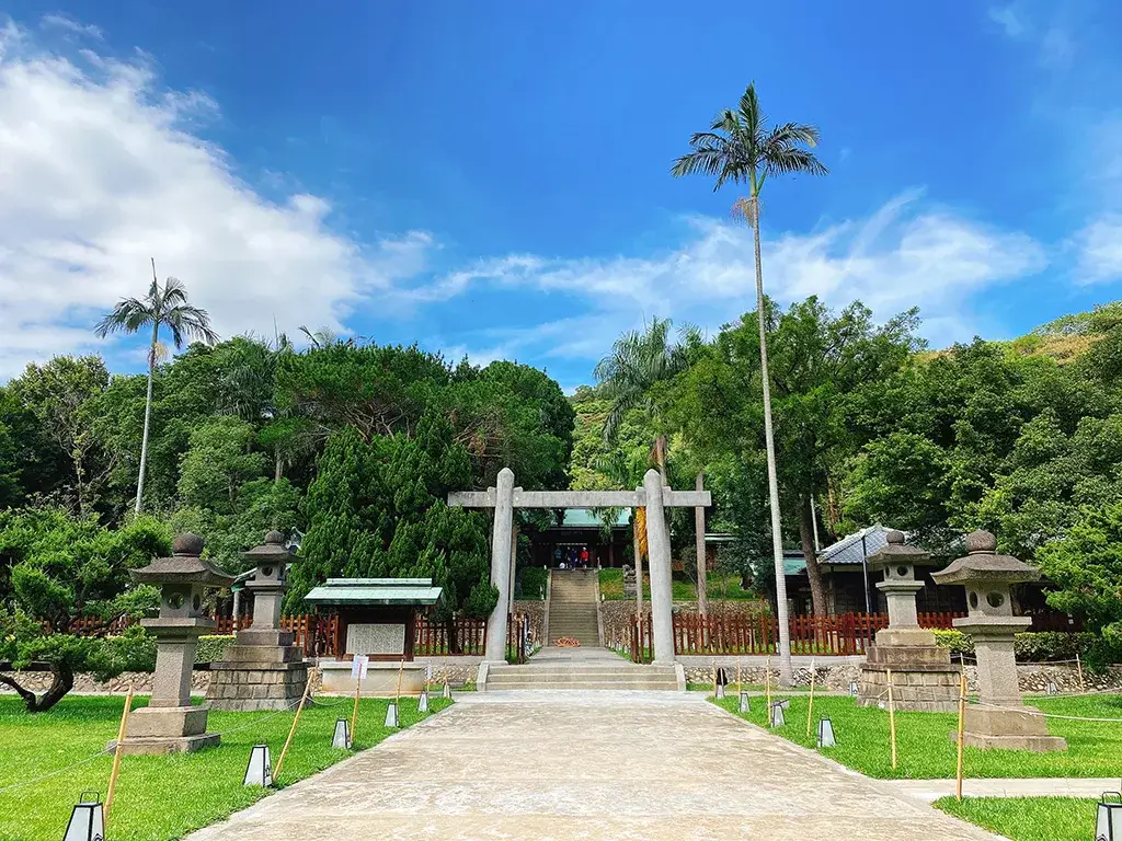 忠烈祠暨神社文化園區石造鳥居與參道石燈，藍天下綠樹環繞。
