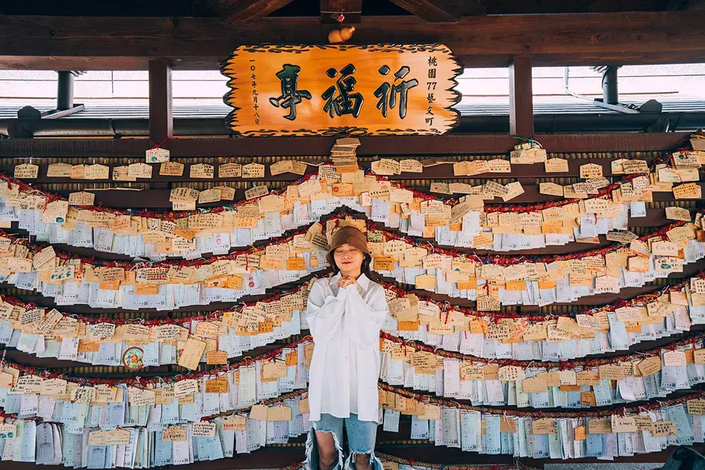 桃園 77 藝文町祈福繪馬牆，遊客站在中央，木牌寫有祈福字樣。