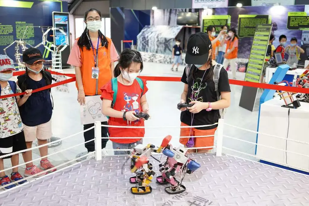 祥儀機器人夢工廠展區，兩名孩童以遙控器操控格鬥機器人在擂台對戰，旁有工作人員與參觀民眾。