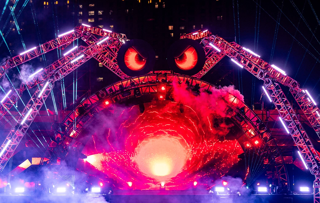 主舞台夜景：拱形燈架與機械蜘蛛手臂，天際光束掃射，兩側LED螢幕播放影像