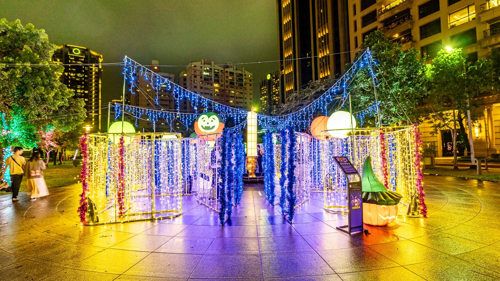 俯瞰發光迷宮裝置，霓虹圍欄與懸掛鬼臉球，中央立柱有行人