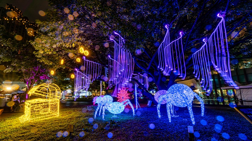 巨樹垂掛粉藍光纖燈，周圍有發光蜘蛛與蛛網裝置